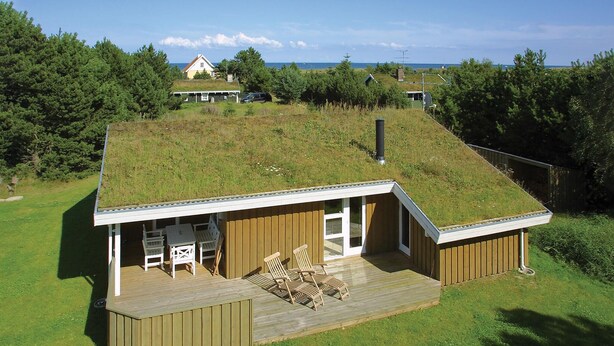 Una casa moderna con techo cubierto de césped, una terraza de madera y un pequeño patio con mobiliario exterior.