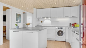 Una cocina moderna con armarios blancos, lavadora integrada y una isla central con frutero.