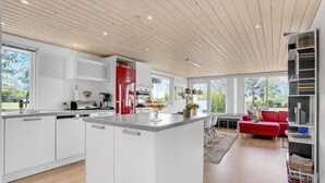 Una cocina moderna con armarios blancos, un refrigerador rojo e una isla central con fruteros.