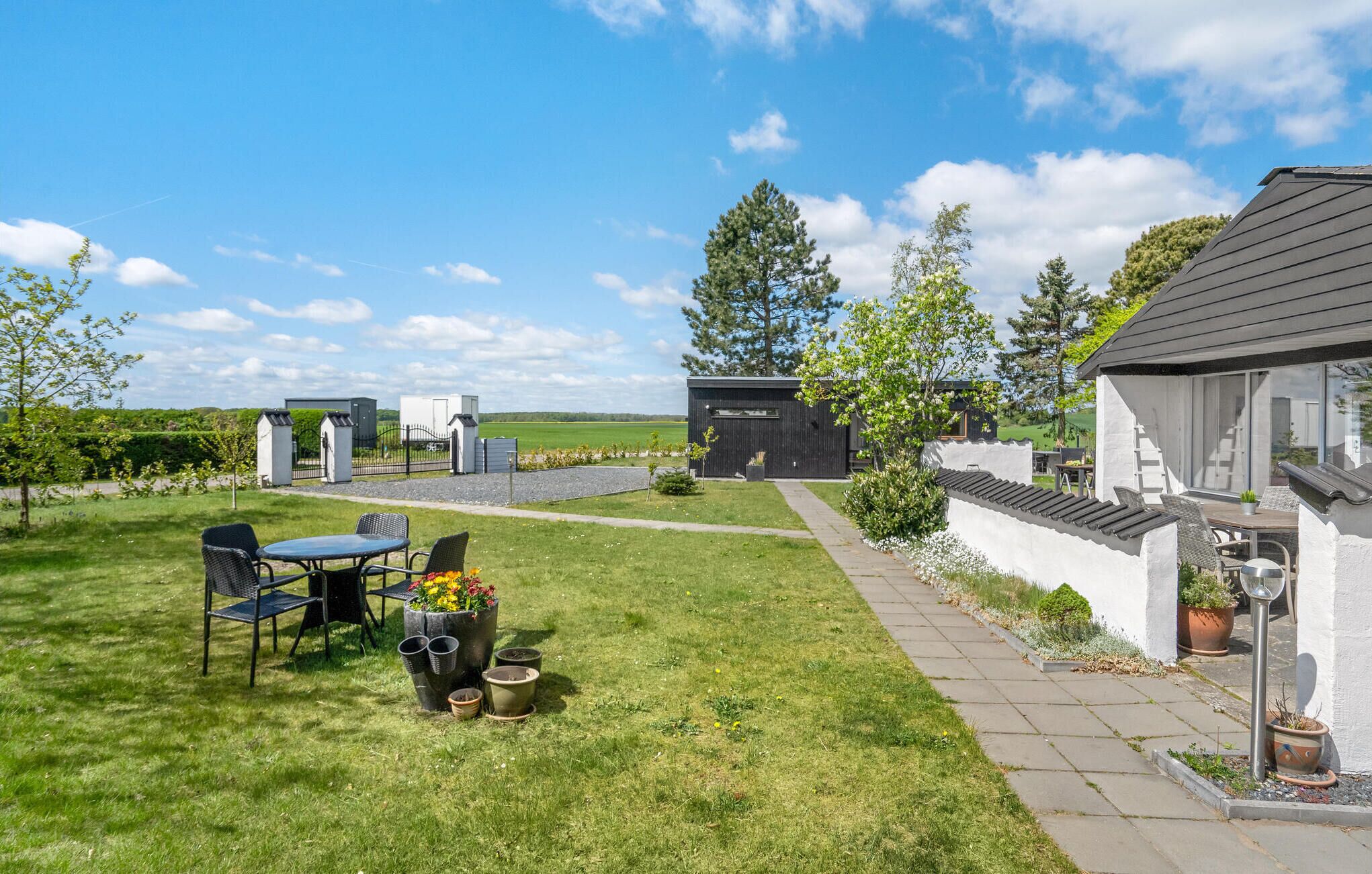 Ein moderner Sitzbereich im Freien mit Tisch und Stühlen, umgeben von einem gepflegten Rasen und Blumentöpfen.