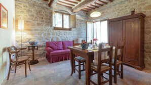 Un comedor rústico con paredes de piedra, vigas de madera, una mesa de madera y un sofá morado.