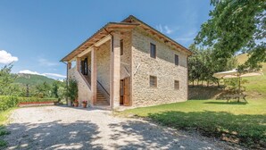 Una casa de piedra con una escalera de madera, un camino de grava y un césped con árboles.