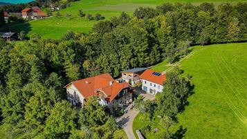 An aerial view of a rural property with two main buildings, surrounded by lush greenery and a clear sky.