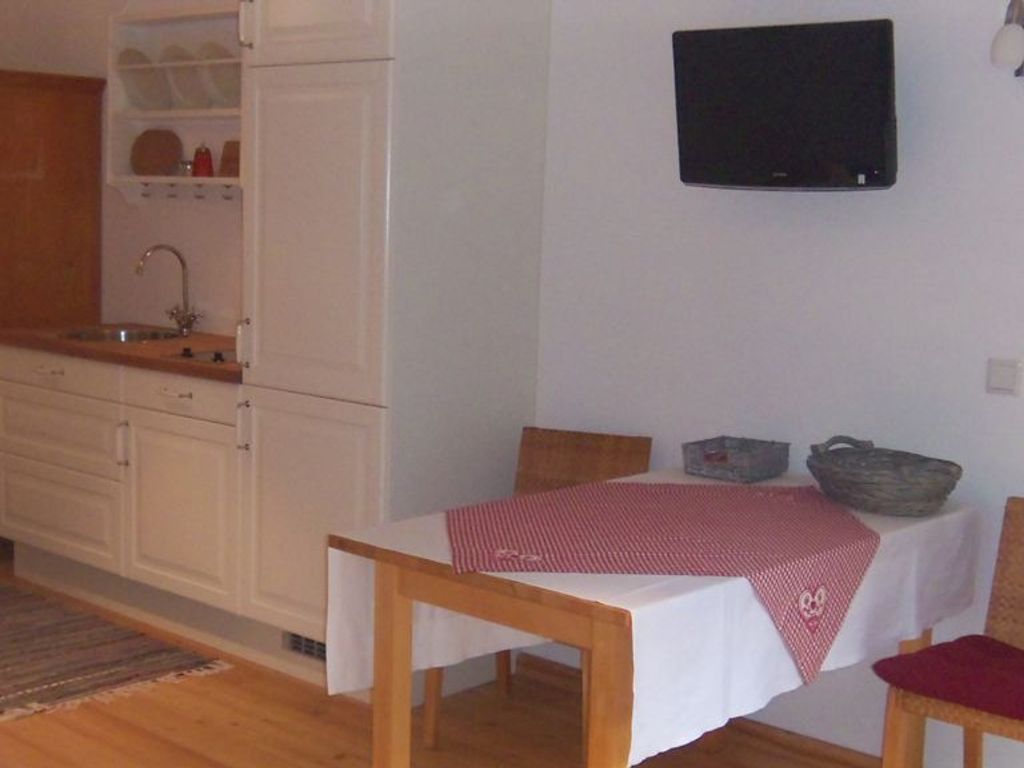 Ein Zimmer mit Esstisch, Wandfernseher, Küchenzeile mit Schränken und Spüle sowie Holzboden.