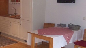 Une pièce comprenant une table à manger, un téléviseur fixé au mur, un coin cuisine avec des placards et un évier, et un plancher en bois.