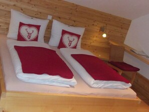 Une chambre de style cabane en bois, avec deux lits, chacun recouvert d’une couverture rouge et agrémenté d’oreillers en forme de cœur.