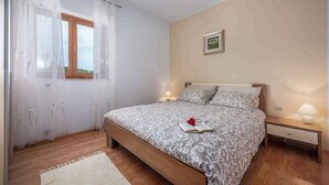 Ein Schlafzimmer mit einem Bett, Nachttischen, einem Fenster mit Vorhängen und einem Wandbild.