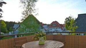 Ein runder Holztisch mit Metallbeinen, begleitet von zwei Stühlen, auf einem Balkon mit Holzlattenzaun.