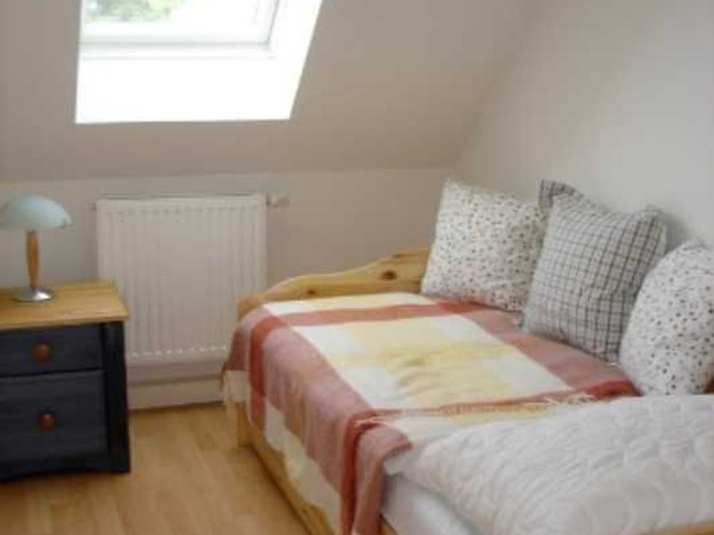 Ein Schlafzimmer mit einem Bett, einem Nachttisch, einer Lampe und einem Fenster.