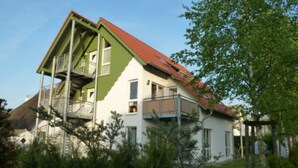 Ein zweigeschossiges Haus mit grüner und weißer Fassade, einem roten Dach und einem Balkon im oberen Stockwerk.