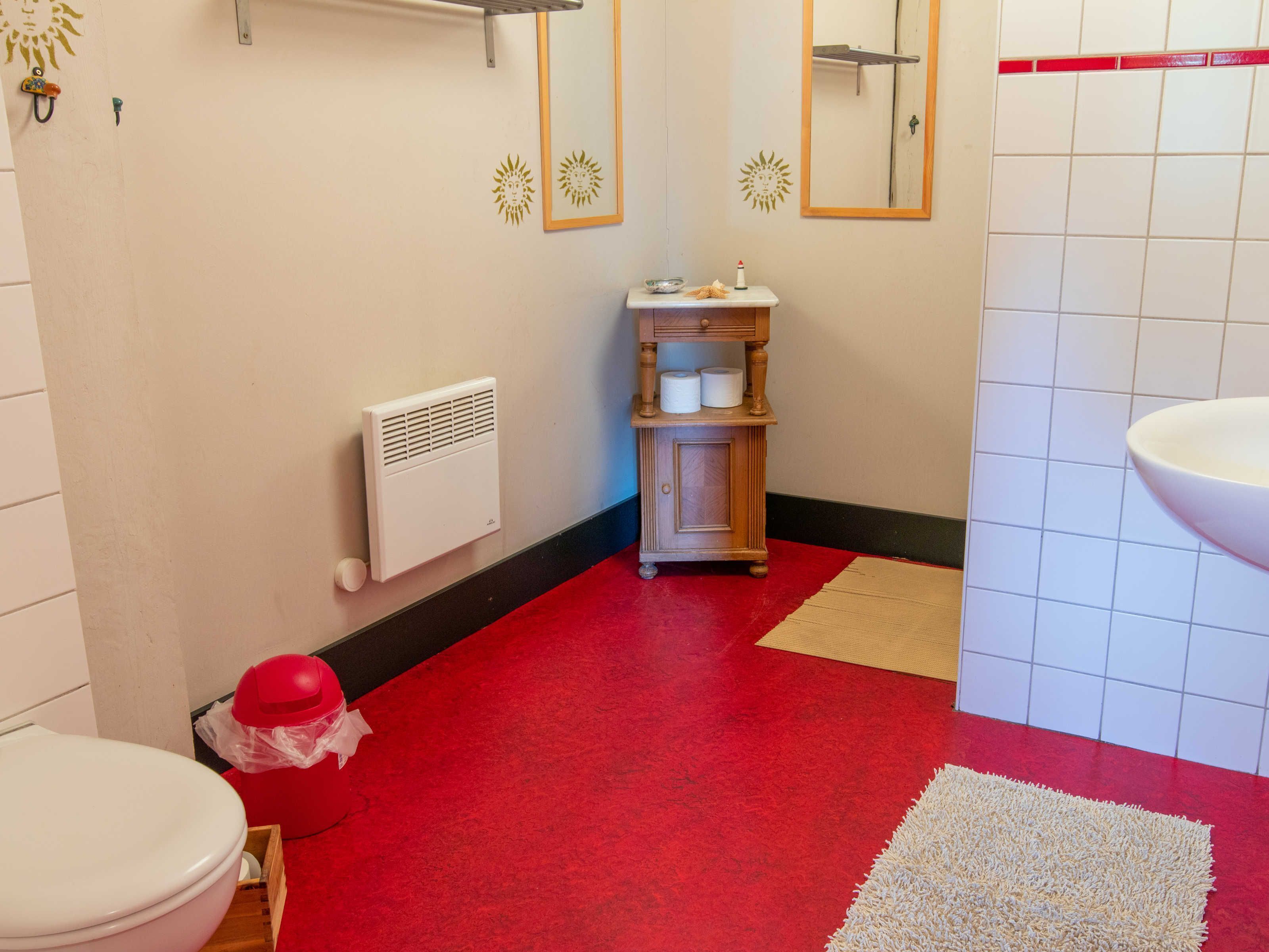 A bathroom with a red floor, a white radiator, a wooden cabinet with toiletries, a white sink, and a mirror.