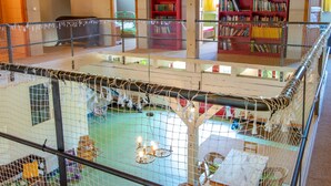 A multi-level indoor space with a netted play area, a staircase, and a library with red bookshelves. - 270m² apartment - apartment (Rubenow)
