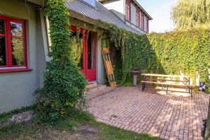 Une maison avec une porte et des fenêtres rouges, une terrasse en briques et un banc en bois.