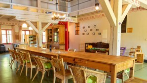 A spacious dining area with a long wooden table and wicker chairs, a kitchen area with wooden cabinets, and a loft space with a netted ceiling. - 270m² apartment - apartment (Rubenow)
