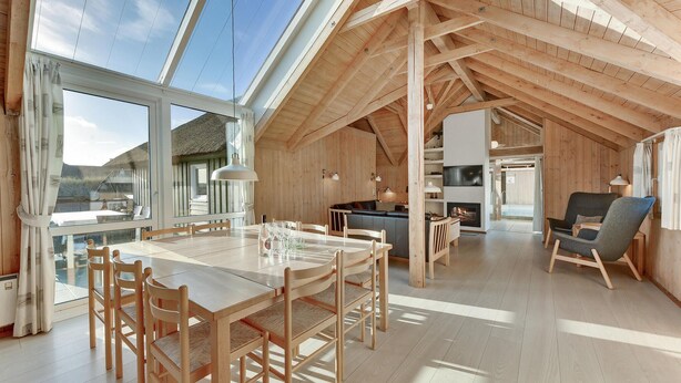 A spacious attic room with a high ceiling, wooden beams, a dining area with a table and chairs, a seating area with a sofa, and a fireplace. - Stunning home in Hvide Sande with sauna (Hvide Sande)