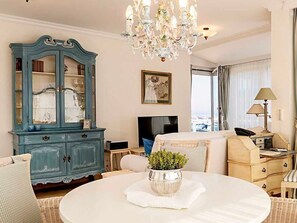 Une pièce comprenant une table à manger, un buffet bleu, un lustre, un téléviseur et une fenêtre avec des rideaux.