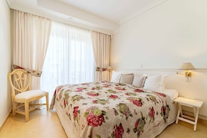 A bedroom with a bed, a chair, a nightstand, and a window with curtains.