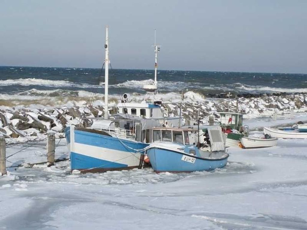 Ein Boot liegt in einem zugefrorenen Hafen mit felsigen Ufern und rauem Meer im Hintergrund.
