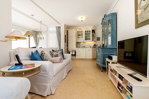 A living room with a sofa, a coffee table, a television, and a kitchen area with cabinets and a blue cabinet.