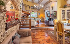 A spacious living area with a stone wall, a wooden staircase, a sofa, a dining table, and a chandelier. - Awesome home in Orgon (Orgon)