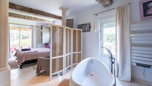 Une chambre spacieuse avec un grand lit, un dressing et une salle de bain dotée d’une baignoire sur pieds.