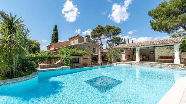 Une piscine d’un bleu éclatant, entourée de bâtiments en pierre dotés d’espaces de détente en plein air et d’une végétation luxuriante.