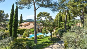 Une villa avec piscine, entourée d’une végétation luxuriante et de grands arbres.