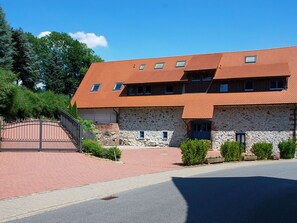A two-story stone building with a red-tiled roof, a gated entrance, and a paved driveway.