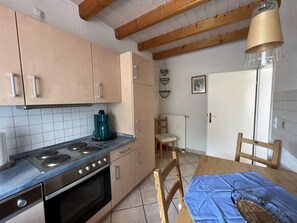 Una cocina con estufa, horno y cafetera en la encimera. Hay una mesa de comedor con sillas y mantel azul.