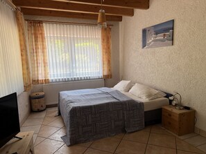 Un dormitorio con cama, mesita de noche de madera, televisor y ventana con cortinas.