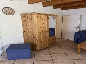 Une armoire en bois avec un miroir, un banc bleu et une porte dans une pièce dont le sol est recouvert de carreaux.