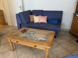 Een woonkamer met een blauwe bank, een salontafel met glazen blad en een houten kast.