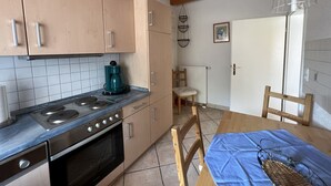 Una cocina con estufa, horno y cafetera en la encimera. Hay una mesa de comedor con sillas y mantel azul.