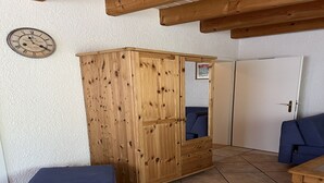 Un armario de madera con espejo, un banco azul y una puerta en una habitación con suelo de baldosas.