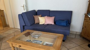 Una sala de estar con un sofá azul, una mesa de centro de vidrio y un mueble de madera.