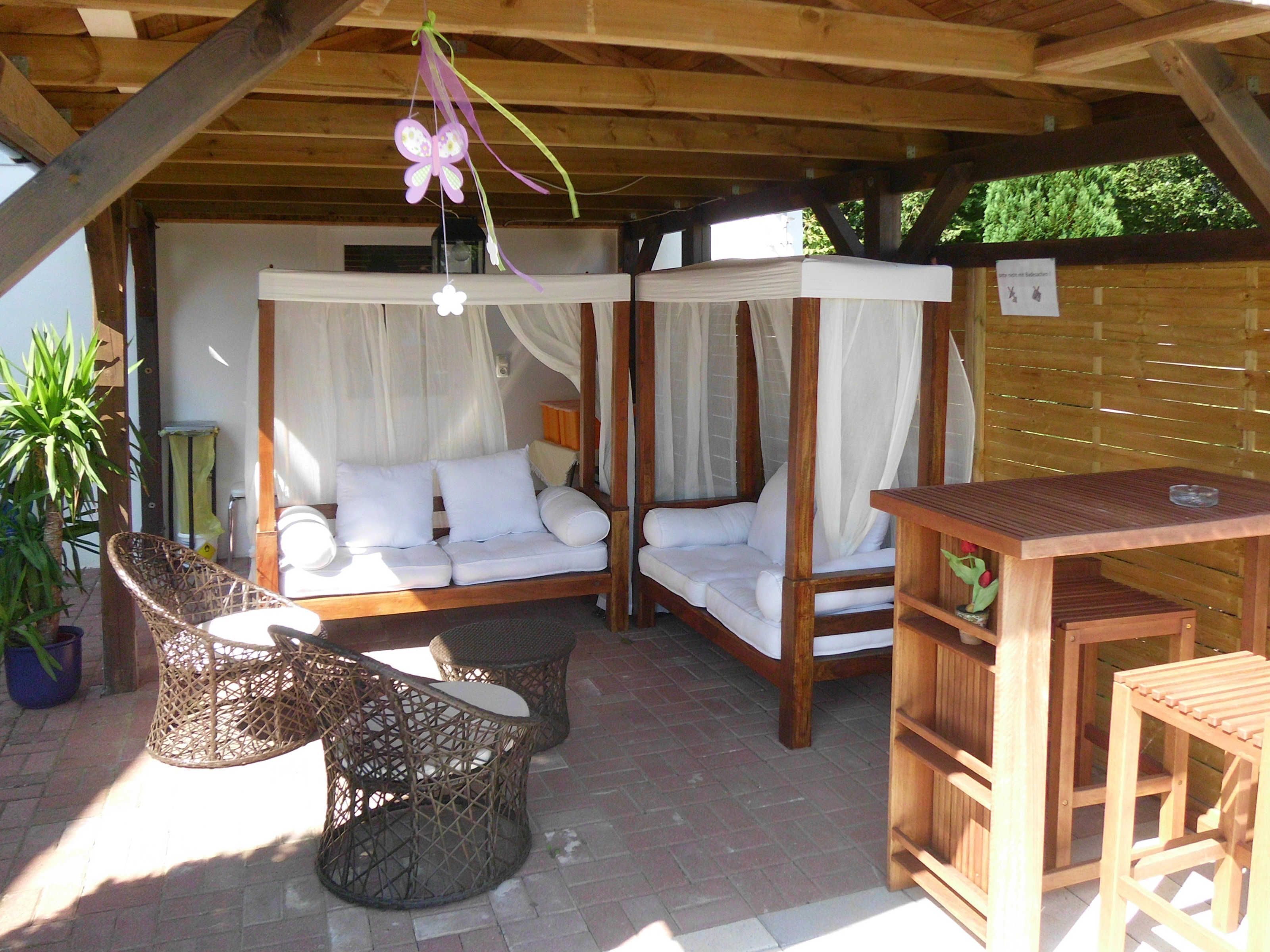 Un espace extérieur abrité, aménagé avec deux bancs rembourrés, des chaises en osier et une table en bois.
