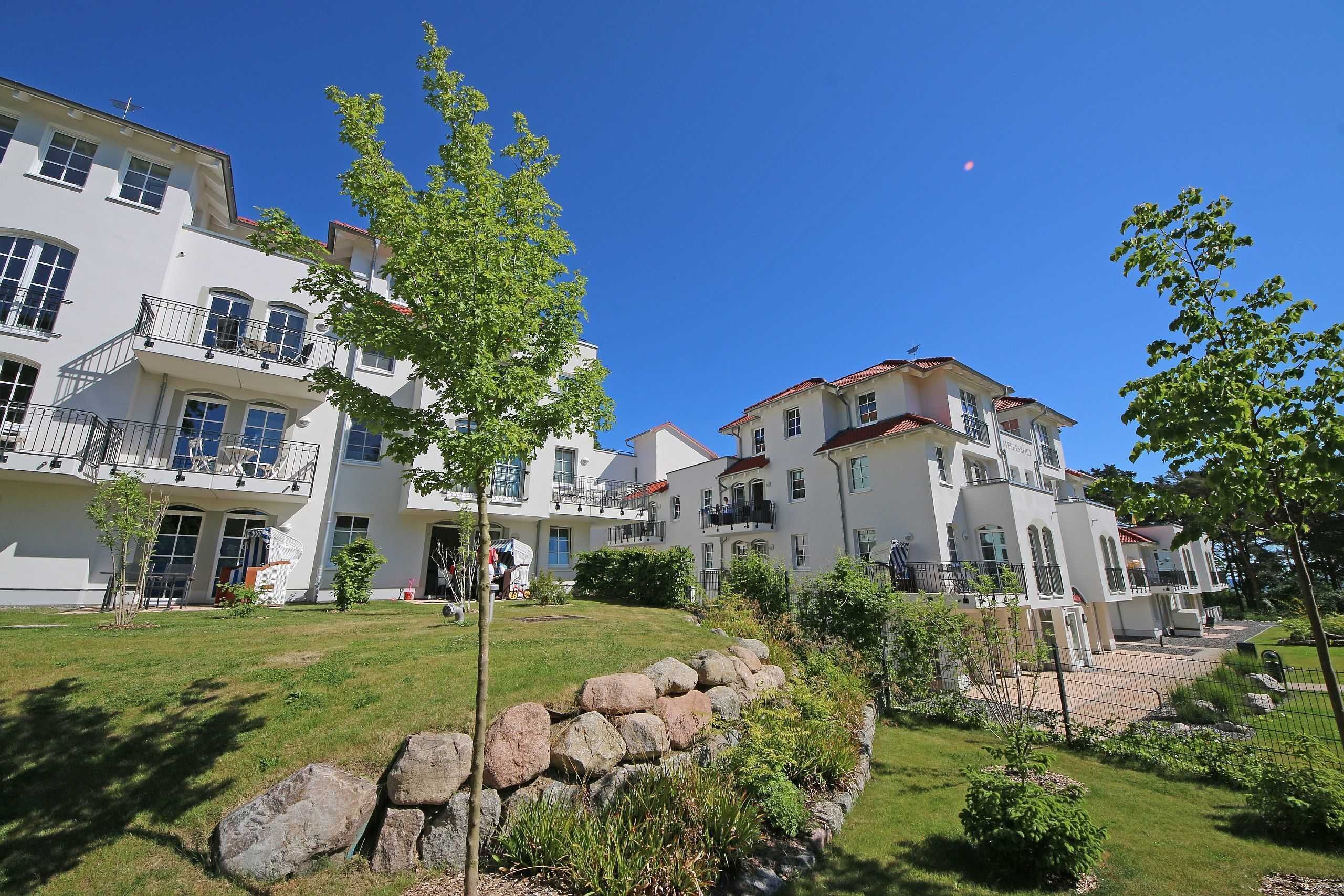 A multi-story residential building with balconies, a well-maintained lawn, and a stone retaining wall.