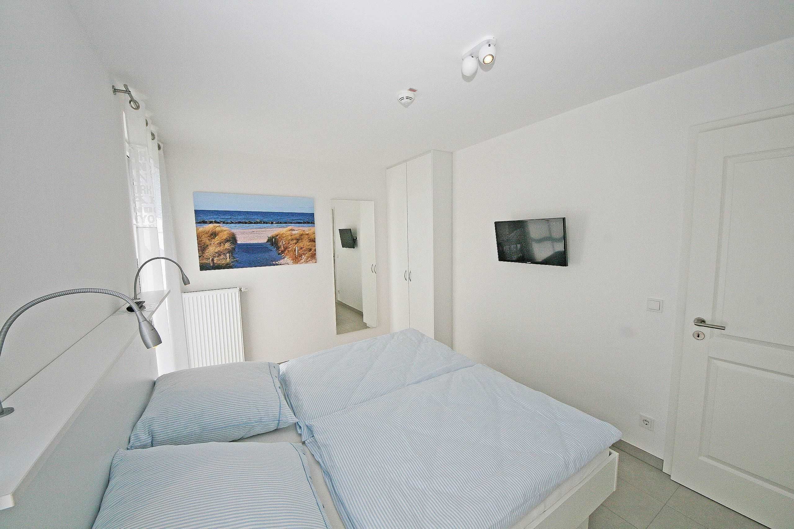 A bedroom with a bed, a bedside lamp, a painting, a television, and a door.