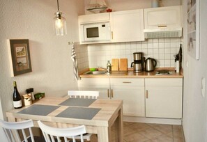 Uma cozinha compacta com armários brancos, micro-ondas, cafeteira e mesa de jantar com cadeiras.