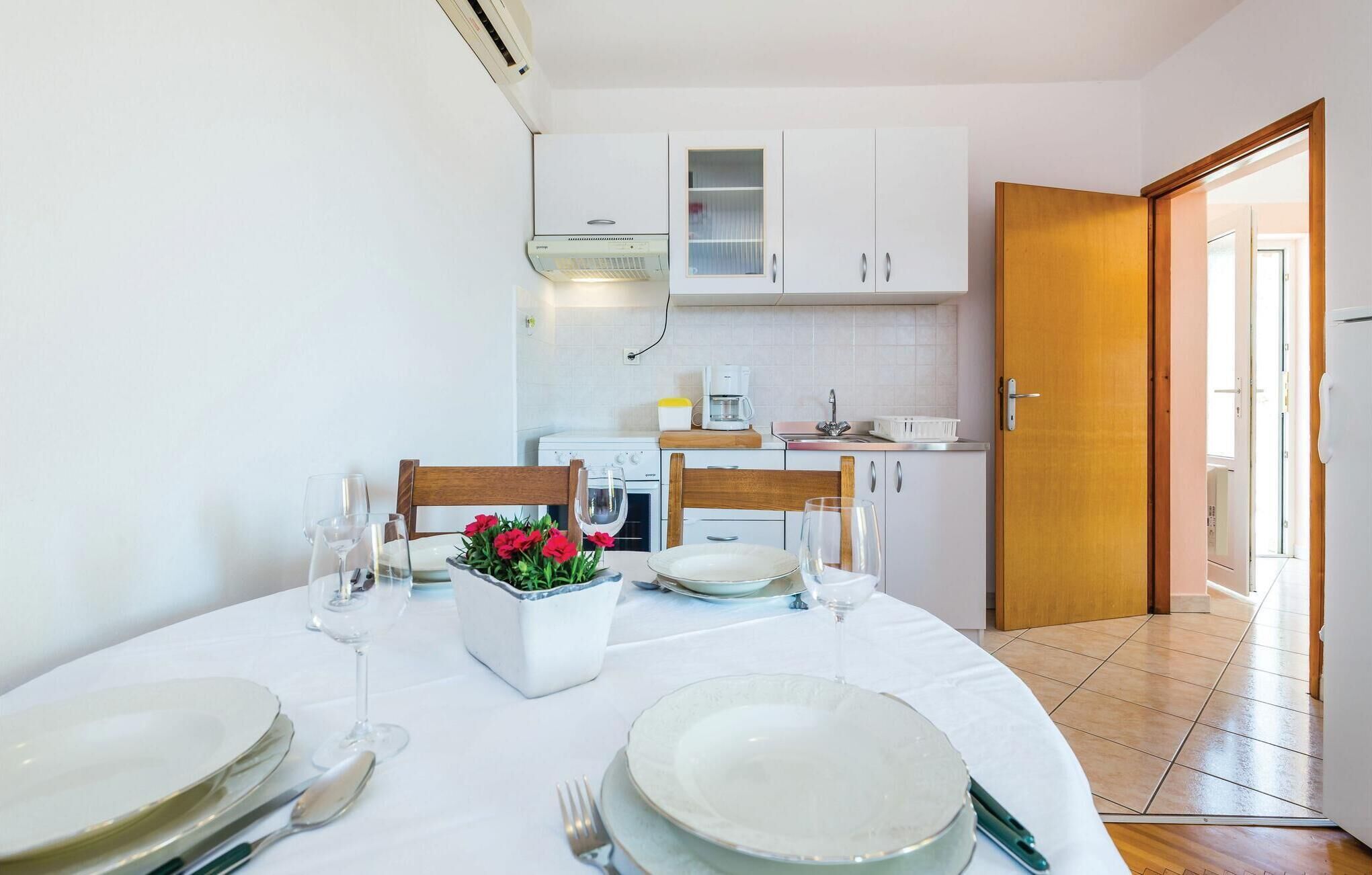 Un comedor con una mesa redonda dispuesta para cuatro personas, armarios blancos, una cafetera y una puerta de madera que da a otra habitación.