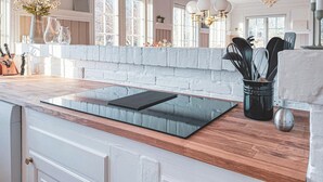 A modern kitchen with a built-in induction cooktop, wooden countertop, and a white brick backsplash.