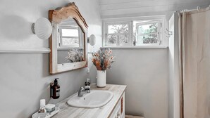 A bathroom with a wooden vanity, a white sink, a large mirror, a window with a view of trees, and a shower curtain.