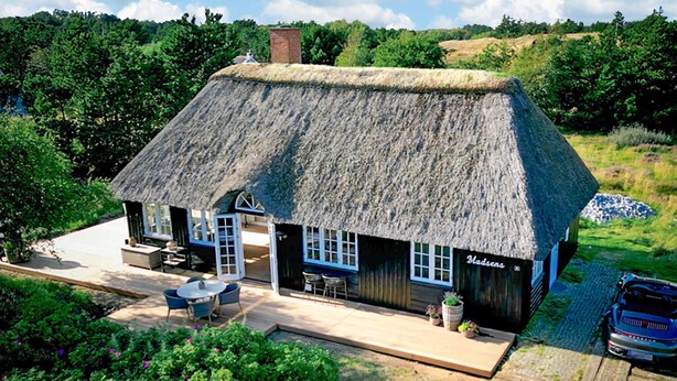 A thatched-roof building with a patio area, a sign reading "Badsens," and a car parked nearby.