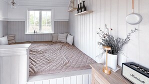 A bedroom with a large bed, a window with a view, a shelf with candles, and a vase with plants.
