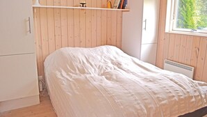 Un dormitorio con cama, una estantería llena de libros, una lámpara y un ventanal con vistas a árboles.