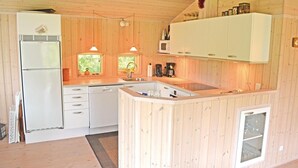 Una cocina compacta con paredes de madera, un refrigerador empotrado, un microondas y un lavamanos.