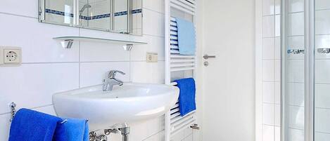 Un baño moderno con un lavamanos blanco, un espejo grande y una cabina de ducha de vidrio.
