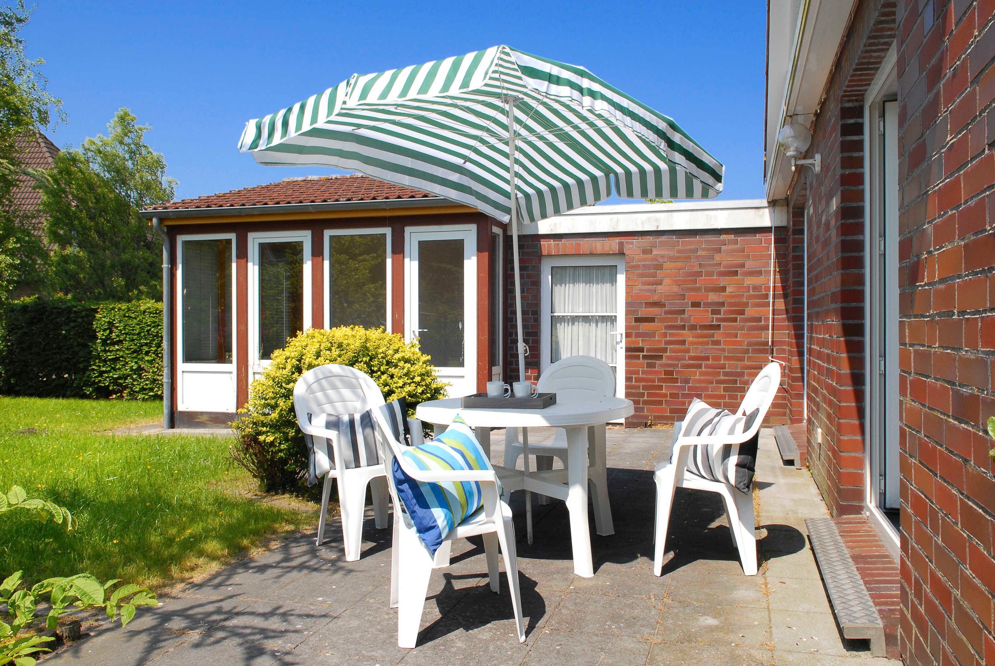 A patio with a table and four chairs, a striped umbrella, and a brick building in the background.