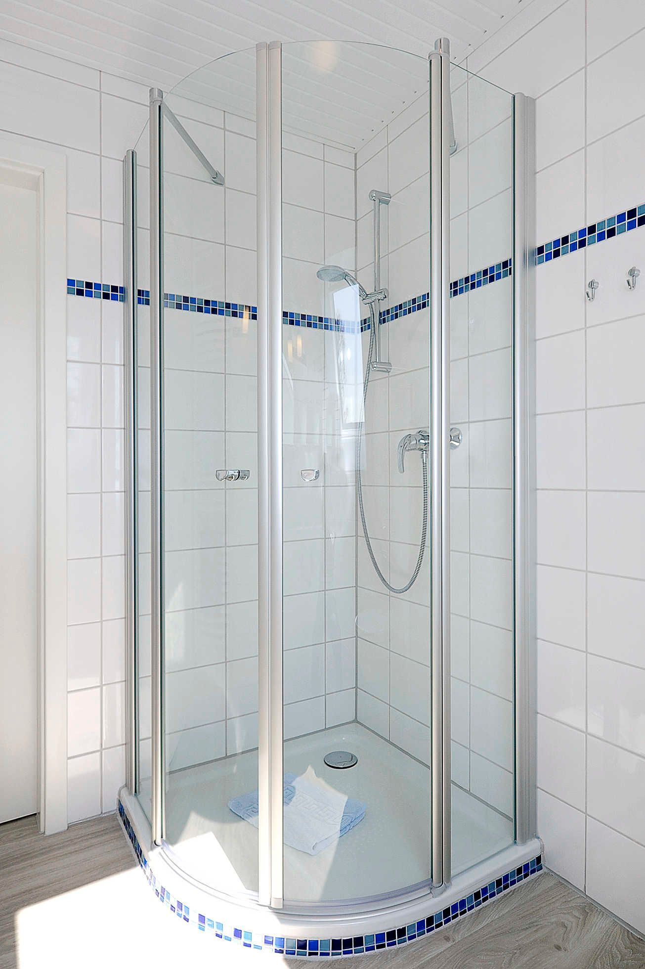 A glass-enclosed shower with a handheld showerhead and a wall-mounted faucet.