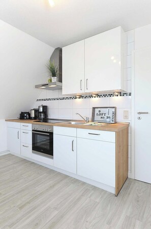 Une cuisine moderne avec des meubles blancs, un plan de travail en bois, un four encastré et une machine à café.